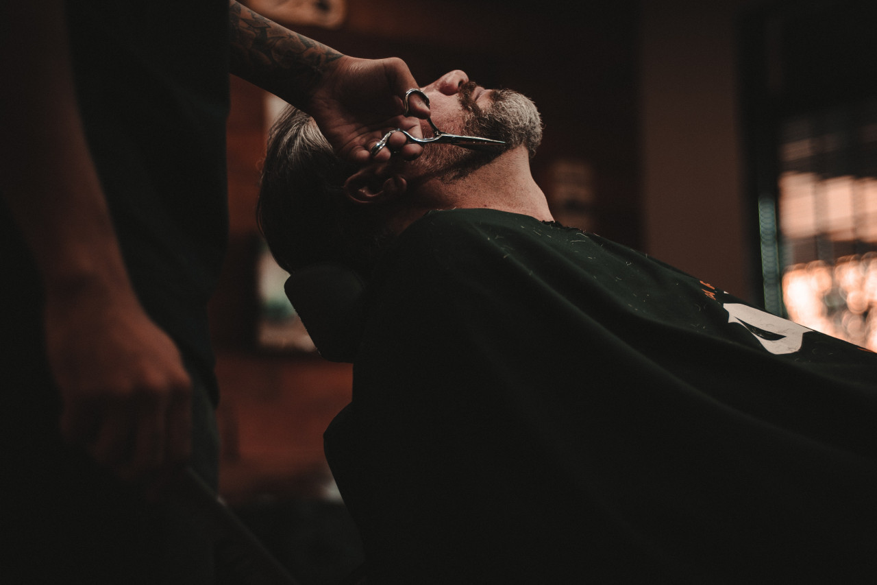 *entretien barbe*  un homme se fait tailler la barbe aux ciseaux, installé dans un fauteuil