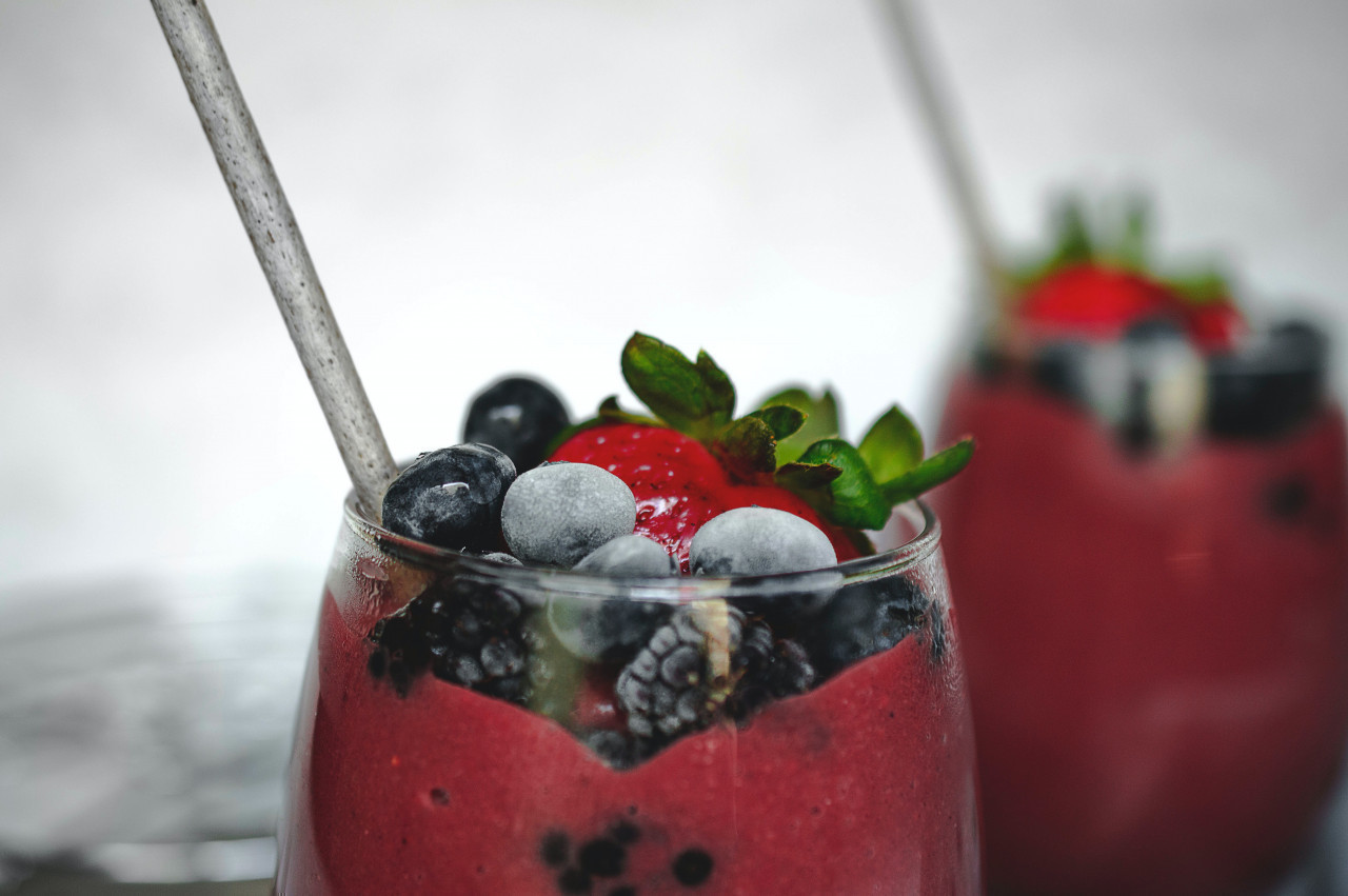 smoothie fruits Un verre avec un smoothie rouge sur lequel reposent des fruits rouges + une paille