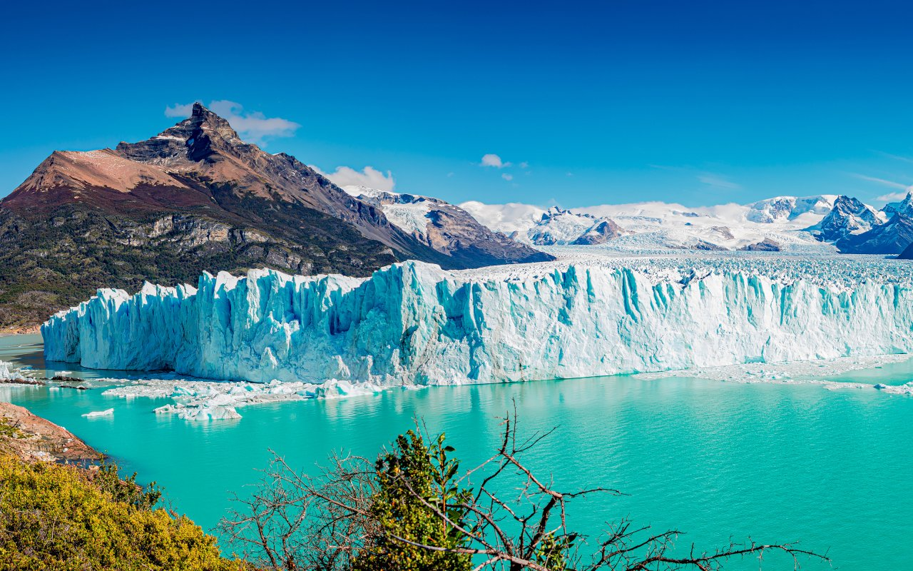 Argentine - eau turquoise sur laquelle flotte un gros glacier avec des montagnes verdoyantes en fond